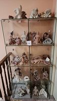 Glass display case with three shelves and multiple ceramic sculptures inside, viewed from the side near a wooden railing.