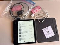 Full view of Kobo eReader screen showing book library interface, two USB chargers, and grey folio case.