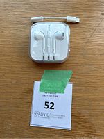 Apple EarPods with Lightning connector in plastic case with in-line remote, displayed on wooden surface with small white Lightning to 3.5mm adapter cable laid nearby.
