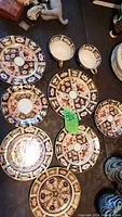 Top-down photo showing a collection of Royal Crown Derby plates and two teacups with intricate Imari pattern designs focussing on the overall set.