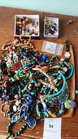 Large assortment of colorful costume jewelry piled on wooden surface, including bead necklaces, bracelets, and a wristwatch.