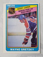 Front of 1983-84 OPC Wayne Gretzky assist leaders hockey card showing image of Gretzky in Edmonton Oilers uniform with bright border.