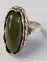 Close-up angle of the elongated oval green jade stone and intricate sterling silver bezel setting of the ring.