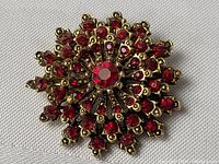 Close-up photo showing detailed red rhinestones and gold-tone burst design of the vintage brooch.