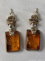 Pair of sterling silver earrings with rectangular amber stones on white fabric background.