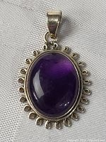 Close-up photograph of the sterling silver pendant with large oval amethyst stone, showing the smooth polished surface of the stone and decorative silver loops around the bezel.