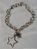 Sterling silver bracelet or anklet with chain links and two star charms on light fabric background