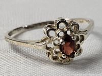 Close-up of the sterling silver ring with oval garnet stone, showing the openwork floral-style bezel and polished band.