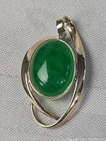 Close-up image of the pendant front showing oval green jade stone in sterling silver setting with curved design.