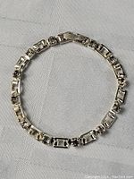 Full view of the sterling silver jeweled bracelet laid flat on a white textured cloth, showing overall shape and design composed of rectangular and round stone settings.