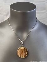 Front view of the silver necklace worn on a mannequin showing the round pendant with layered peach and tan components inside.