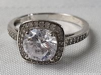 Close-up front angled view of sterling silver ring featuring cushion-cut clear gemstone with decorative bead detailing on square setting.