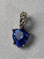 Close-up front image of sterling silver pendant with heart-shaped blue sapphire and three small clear stones on the bail, showing front details and color.