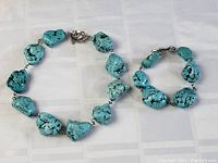 Turquoise necklace and bracelet set arranged on a light surface showing size and stone details.