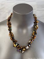 Front view of necklace displayed on grey mannequin showing diverse gemstones including amber and amethyst