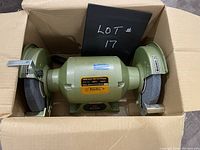 Full view of the Busy Bee bench grinder set inside a cardboard box, showing the grinder's wheels and body.