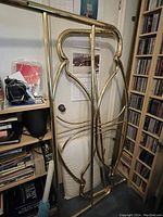 Queen size brass headboard and footboard leaning against the wall in a room with bookshelf and other items.