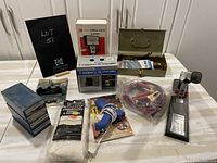 Overview of all items on a table including stapler, glue tool, Dwell-Tach tester, sawhorse brackets box, storage box, jumper cables, and small hand tools