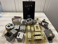 Photo of assorted electrical boxes, switches, outlets, and covers laid out on a table labeled Lot 9