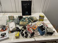 Wide view of assorted electrical supplies on table including switch plates, plugs, conduit fittings, outlets, and wire nuts.