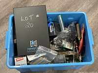 Overview of blue plastic tote filled with assorted hand tools and hardware, featuring hand planer, rivet puncher, sand cloth, drill bits, pliers, and various small tools.