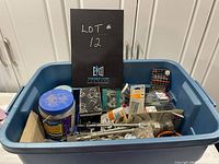 Blue plastic bin filled with assorted screws, nails, wingnuts, drill bits, glazing points, and miscellaneous hardware items. Multiple hardware packages and loose metal pieces visible.