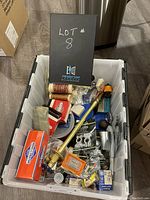 White plastic tub filled with various small hardware items including screws, nails, wire, plumbing fittings and packaged fasteners.