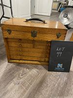 Front view of oak tool chest closed, showing six drawers, brass hardware and leather-wrapped handle