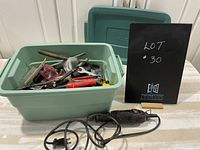 Green plastic bin filled with various un-inventoried hand tools, fasteners, and an electric rotary tool with black cord.