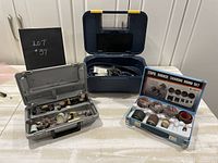 Overall view of the three items including blue metal case with rotary tool accessories, shaft grinder case, and 25pc rubber sanding drum set in its box.