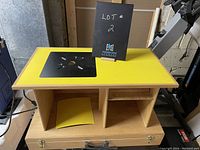 Front and top view of the table saw base showing yellow laminate with black metal center insert and wooden cabinet