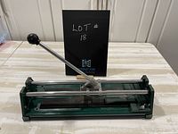 Full view of the manual tile cutter showing its green base, silver rails, and metal handle with black round knob.