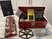 Photo of the open red metal toolbox containing various tools and construction items including a handsaw and boxed hardware items, along with a red tray with hardware parts and a black round tool component.