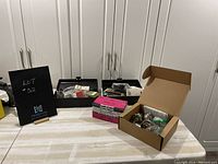 Two small black plastic tool boxes and an open cardboard box showing screws, nails, and door handle components on a table.