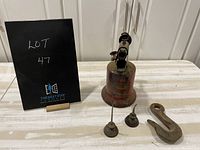 Vintage red metal torch, two small oil cans, and cast iron hook on white surface with black card labeled Lot 47.