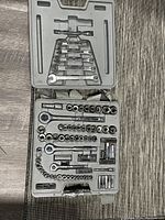 Socket wrench set showing inside of broken plastic case with ratchets, sockets, extension bars, and wrenches arranged inside.