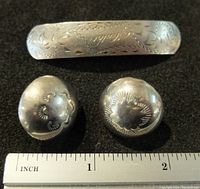 Top view of sterling silver hair barrette with floral engraving and two round clip earrings with floral designs alongside a ruler for scale.