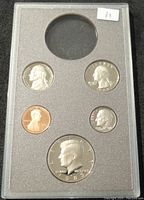 Front side of proof coin set showing five coins: nickel, quarter, penny, dime, and half dollar, with missing silver dollar at top center slot.