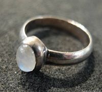 Close-up angled view showing silver band and bezel set milky oval cabochon gemstone.