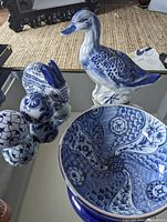 View of blue and white ceramic duck figurine, carpet balls, and bunny dish on reflective glass surface.