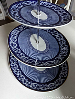 Close-up side view of the three graduated blue and white oval plates with intricate border and central geometric pattern connected by a metal rod.