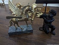 Brass winged pegasus figurine on marble base alongside a figurine of a man holding a card.