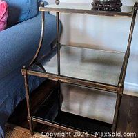 One of the two three-tier side tables showing antique brass finish metal frame and mottled mirrored glass shelves