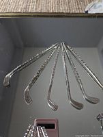 Photo showing six silver plated cocktail sticks shaped like miniature hockey sticks fanned out on a reflective surface.