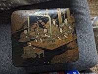 Top view of lacquered box showing detailed painted scene of seated figures in traditional dress inside a room.