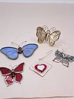 Four assorted butterflies and a heart-shaped glass ornament displayed on a white surface.