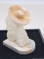Side angle view of carved onyx stone bookend figurine showing the stylized seated person with large hat on base.