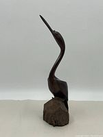 Side view of a carved wooden bird figure with long neck and beak, mounted on a natural wooden block base.