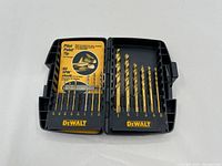 Closed black plastic case contains a set of gold-colored titanium drill bits organized by size with DEWALT logo in yellow printing.