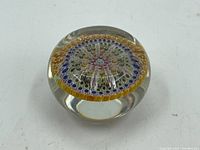Top view of round millefiori paperweight showing detailed colorful floral design in circular pattern with yellow flower petal ring.